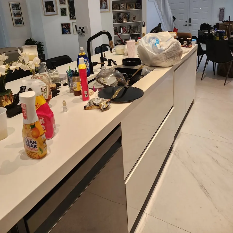 Kitchen island before cleaning, covered in bottles, bags and dishes