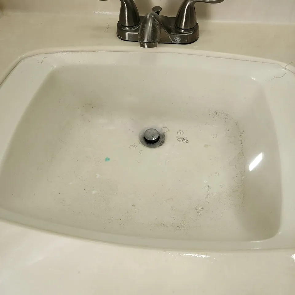 Bathroom sink before cleaning, with soap scum and debris in the basin